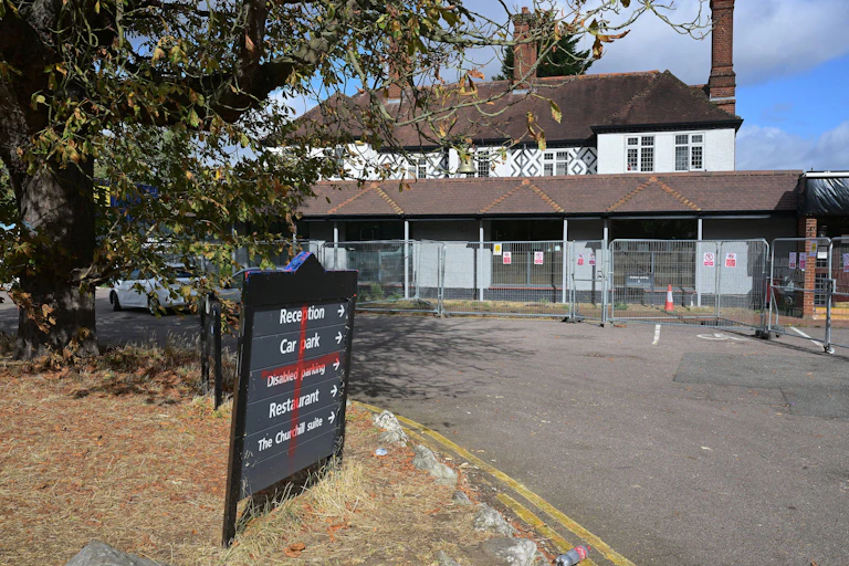 The Bell pub, surrounded by fencing. Someone has painted a red cross on the sign at the front of the building.