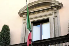An Italian flag bound with a black tie hangs outside a stone house.