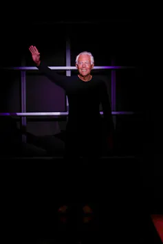 Un hombre vestido de negro saluda.