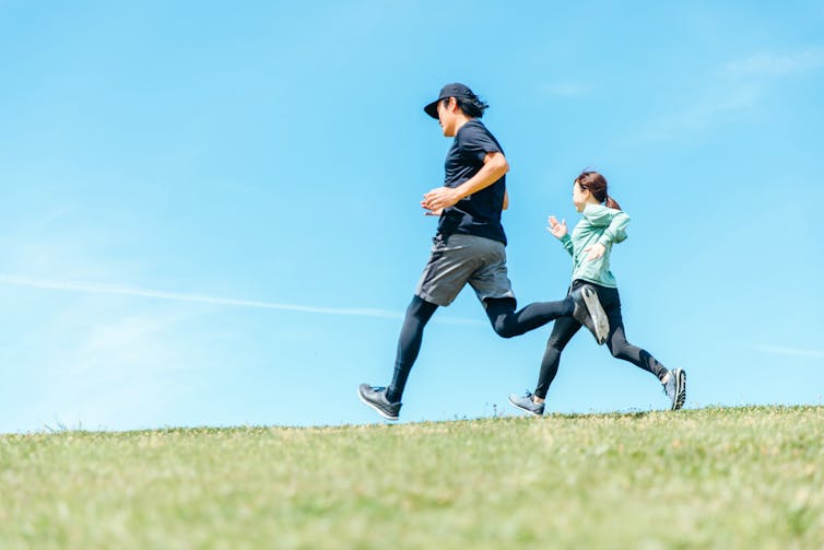 A man and woman in workout clothes run across a grassy field.