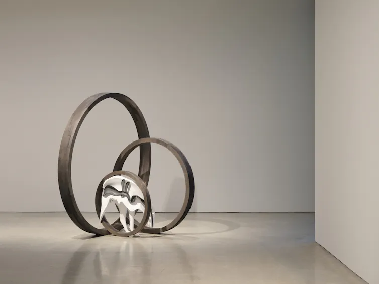 Metal sculpture featuring three intersecting silver rings and white dog