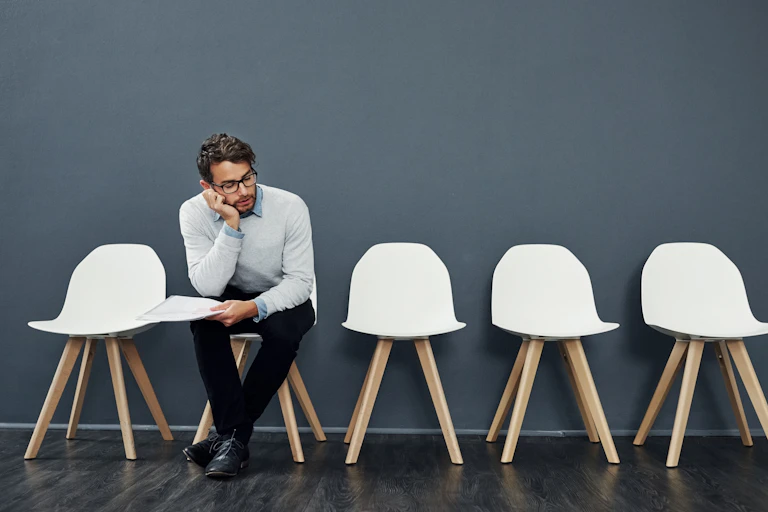 Man holding document sits next to empty chairs.