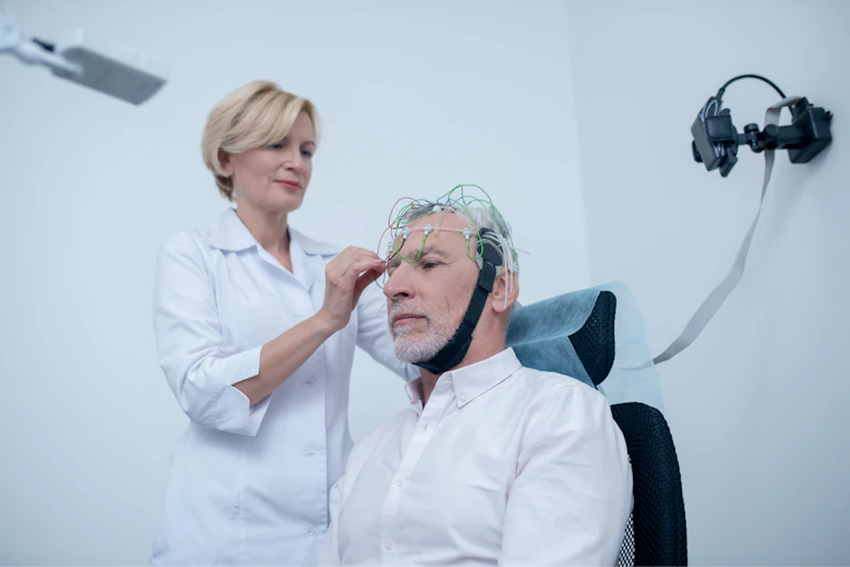 A female doctor applies an EEG cap to an older man's head.