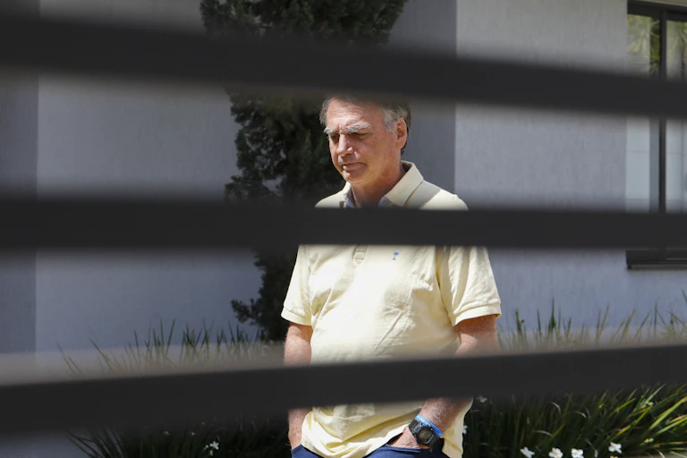 A man in a white shirt is seen behind a blind.