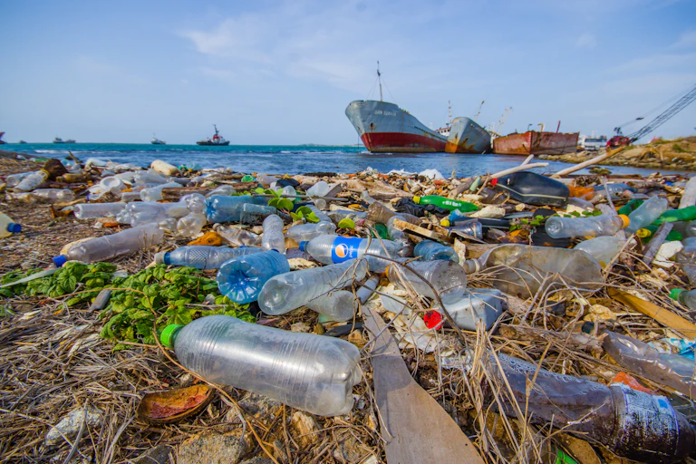Envases de plástico desechados en la costa con barcos en el mar al fondo