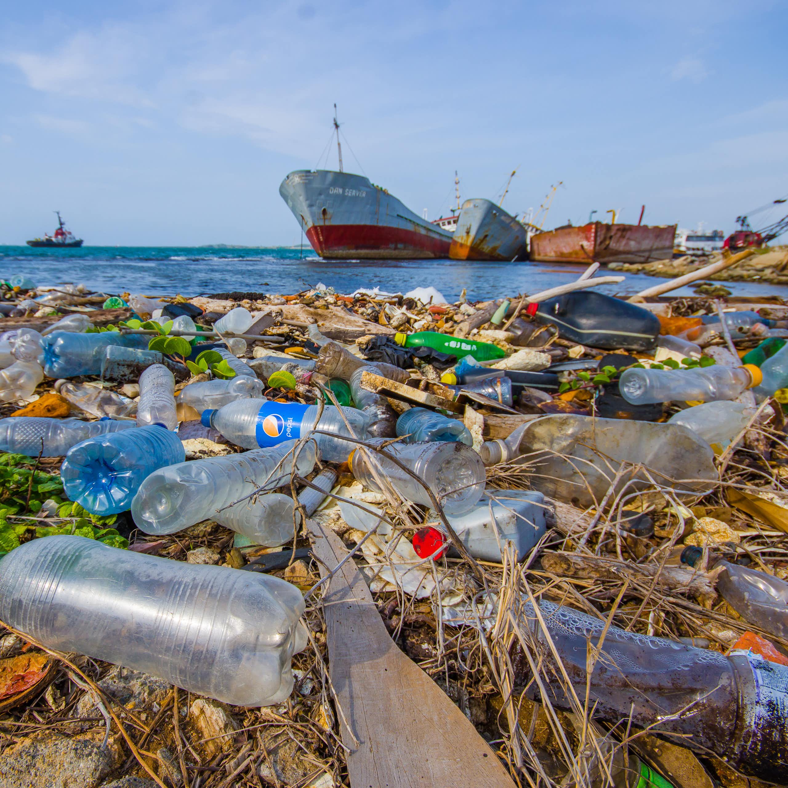 Envases de plástico desechados en la costa con barcos en el mar al fondo