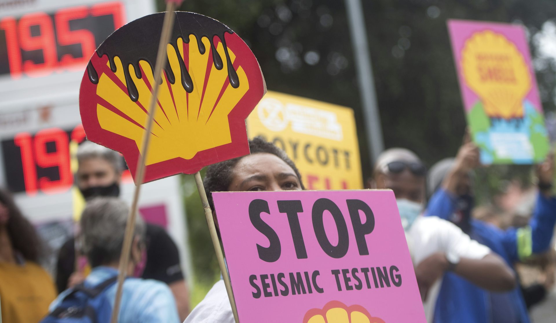 Activists stand outside a Shell petrol station with placards that show shell logo dripping with oil and a sign that says Stop Seismic Testing