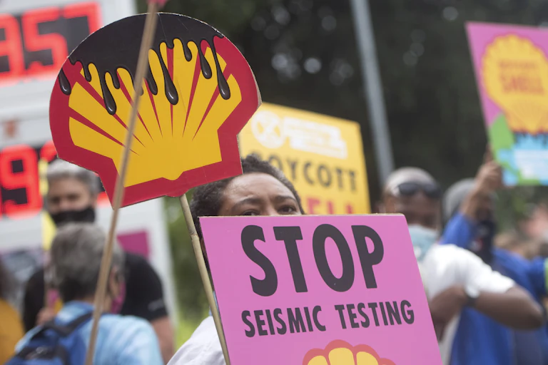 Activists stand outside a Shell petrol station with placards that show shell logo dripping with oil and a sign that says Stop Seismic Testing