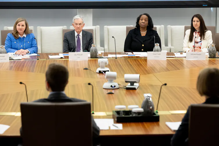Four people sitting at one end of a large wooden table, at a meeting.