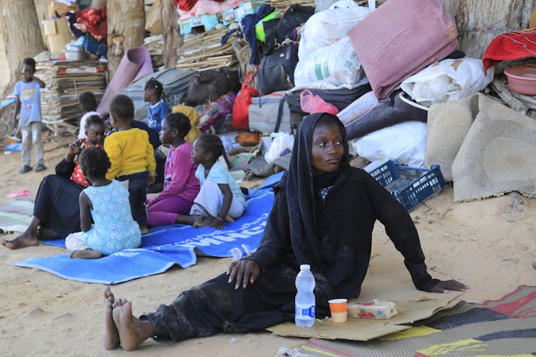 La mujer negra está sentada en el suelo entre otros refugiados reunidos cerca.