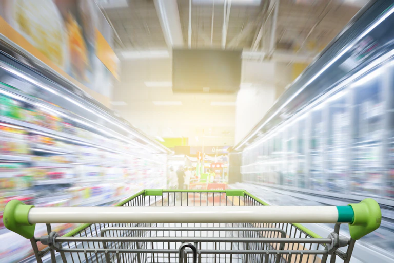 Panorama. Supermarket aisle with empty green shopping cart.