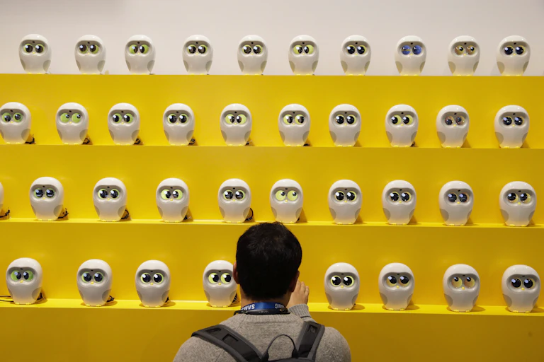a person looks at rows of small white robots placed on yellow shelves