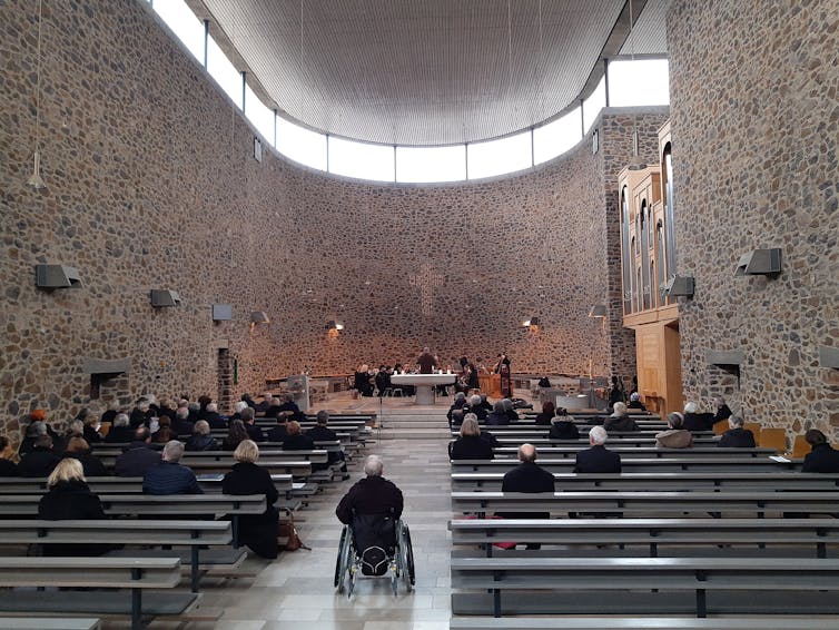 A large, airy and modern-looking sanctuary with a few dozen people in the pews as performers sit behind the altar.