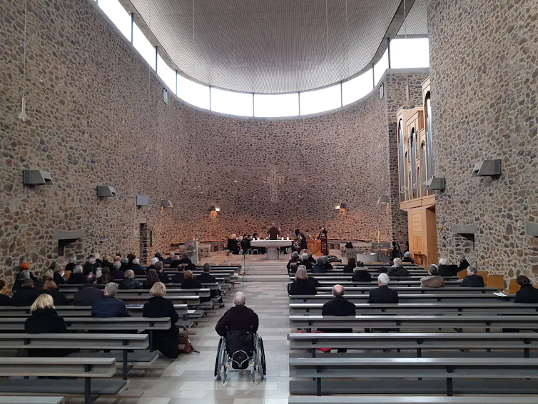 A large, airy and modern-looking sanctuary with a few dozen people in the pews as performers sit behind the altar.