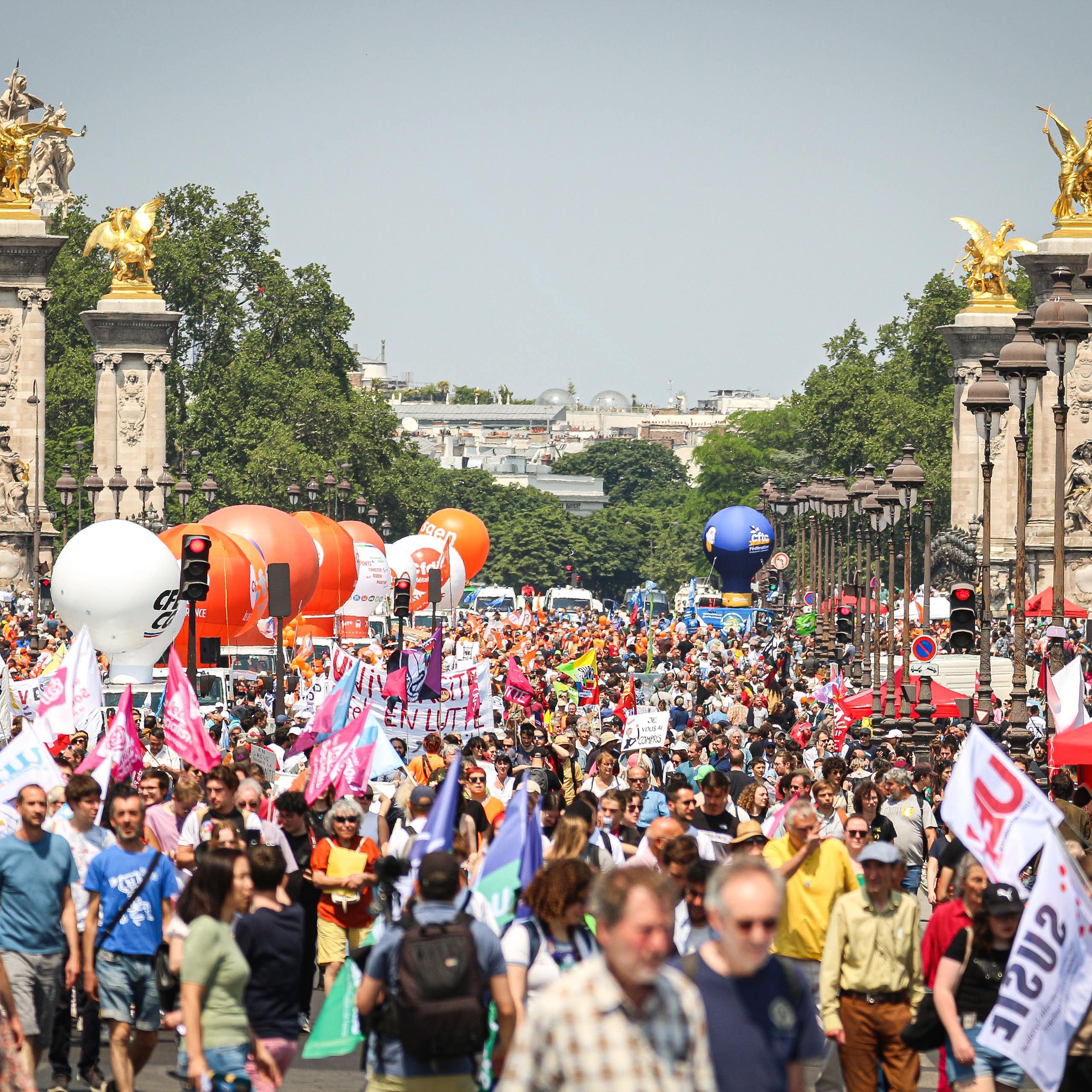 People are visible amid a protest on a sunny day in Paris.