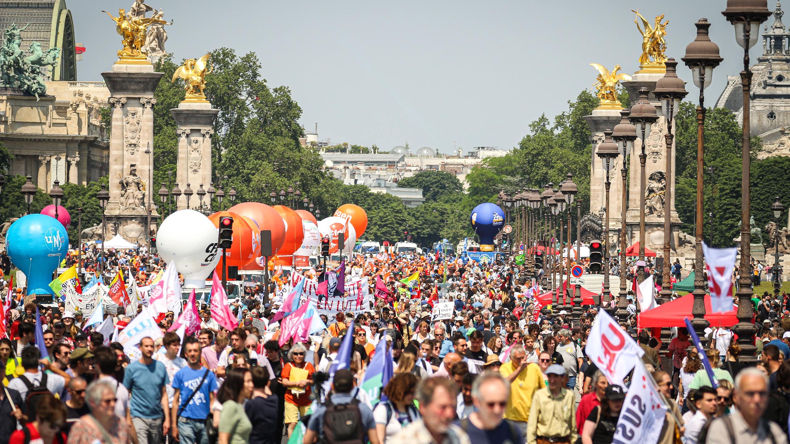 People are visible amid a protest on a sunny day in Paris.