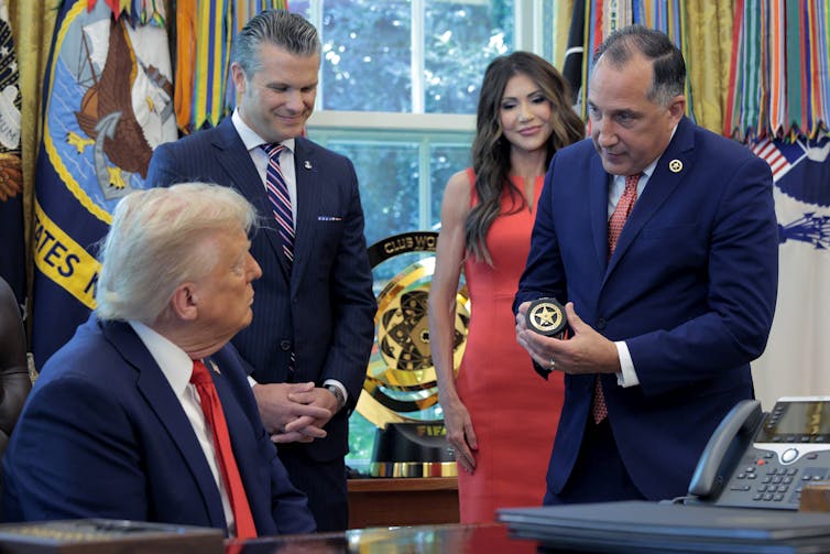 Bail reforms throughout the USA have proven that freeing folks pretrial doesn’t hurt public protection 1 A man presents a badge to another man who is seated, as two other people watch.