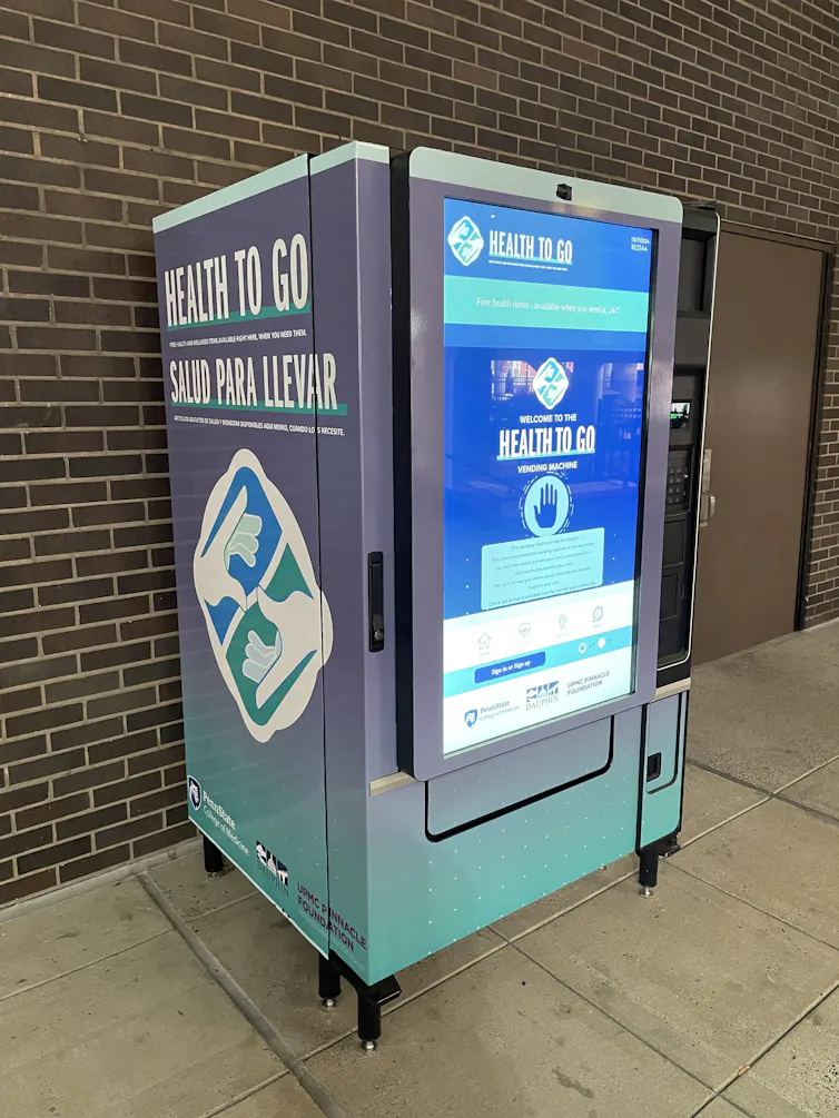 A teal and grey vending machine that says 'Health To Go' with large digital touchscreen on front