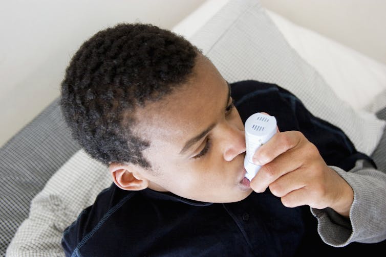 A Black boy holds a medical device in his mouth.