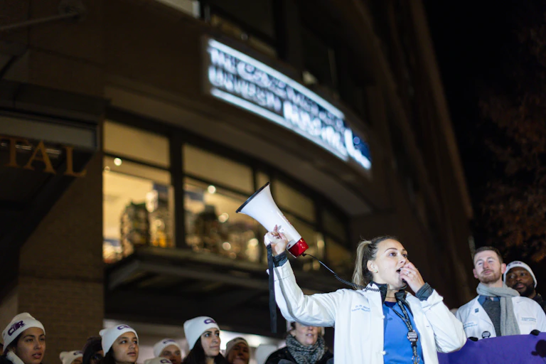 A female doctor waves a megaphone aloft while standing among a group of doctors outside a hospital.