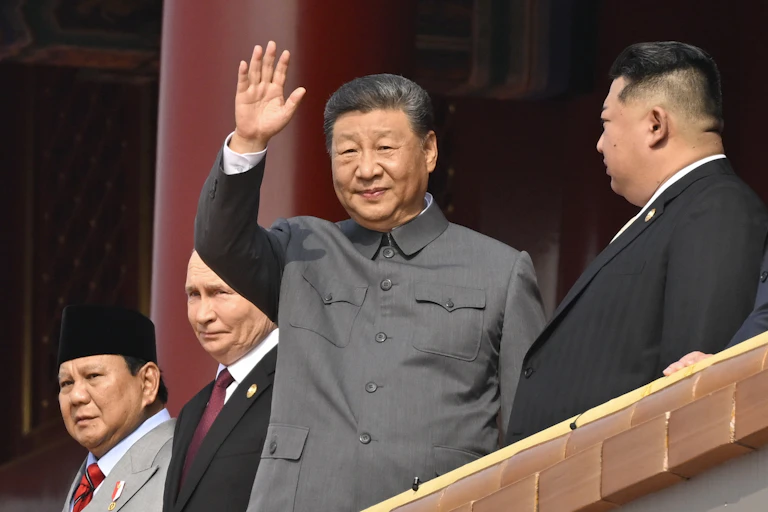 Xi Jinping waves from a platform, flanked by Kim Jong Un and Vladimir Putin