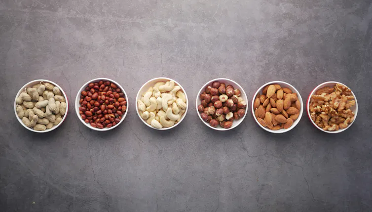 5 bowls of different nuts, including unshelled peanuts.