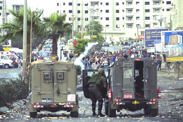 Israeli security forces shelter behind armoured vehicles when confronted by crowds of Palestinian civilians.