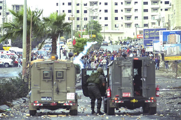 Israeli security forces shelter behind armoured vehicles when confronted by crowds of Palestinian civilians.