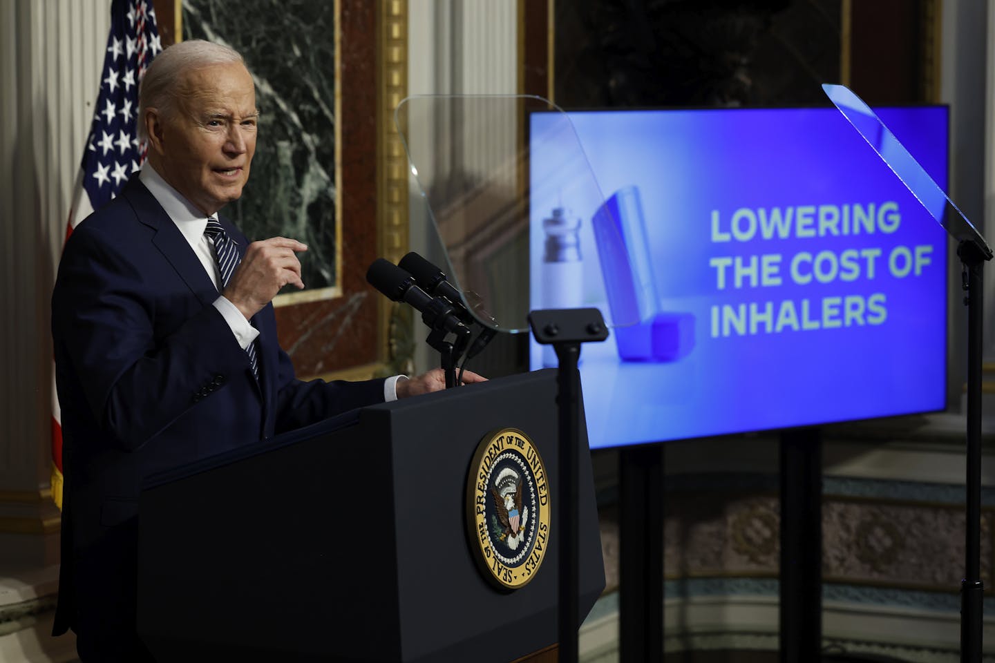 Former president Joe Biden speaks at podium alongside digital screen that says 'Lowering the cost of inhalers'