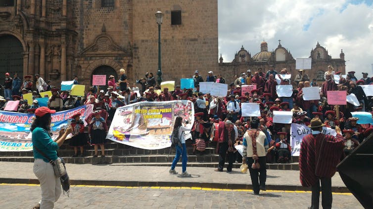 Grupo de personas con pancartas reunidas en una escalinata frente a una catedral