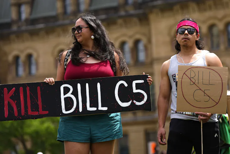 Una mujer con cabello largo y oscuro contiene un letrero que decía matar fue C-5 como un hombre en el pañuelo de pie junto a ella.
