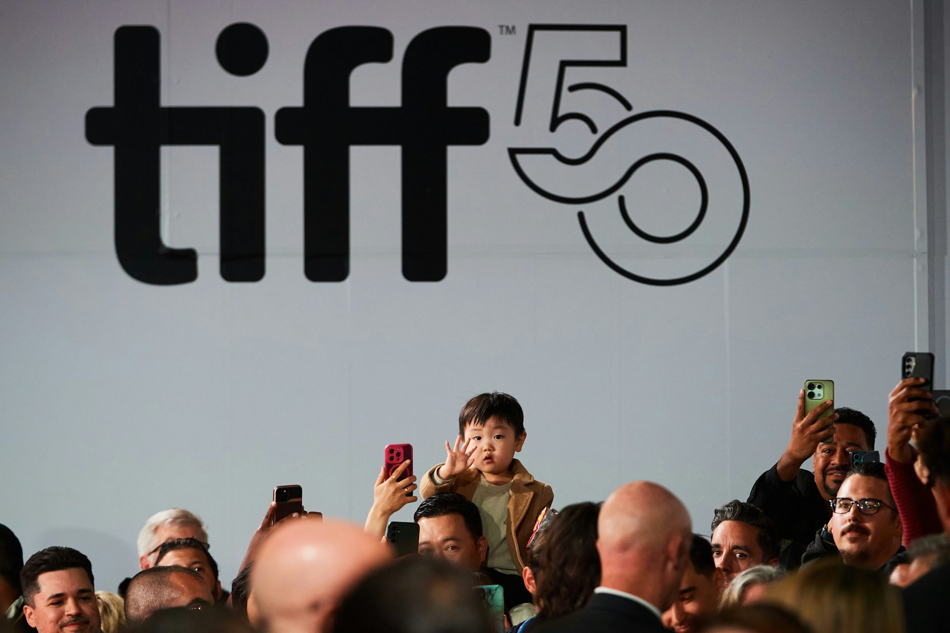 Personas que saludan en una multitud, incluido un niño pequeño sobre los hombros.