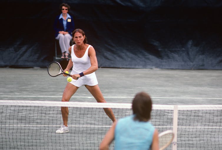 A transgender woman plays tennis on a clay court.