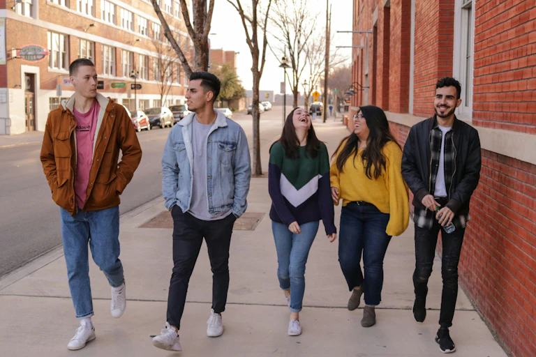 A group of five young people walking down a street and smiling