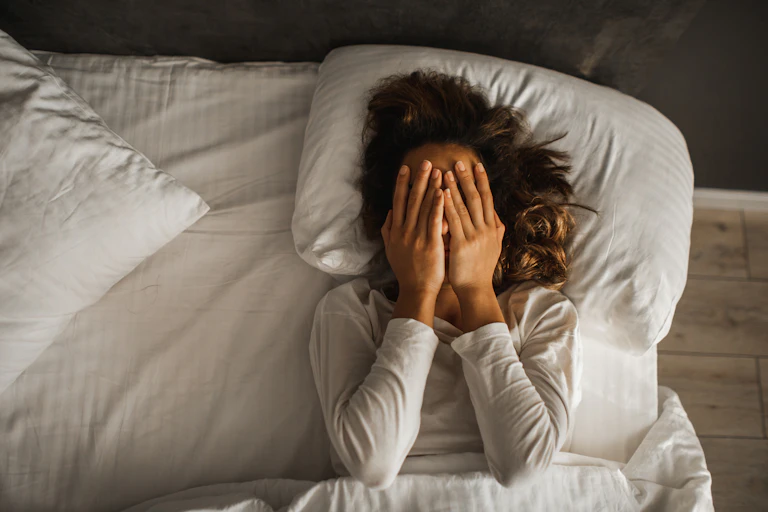 Woman lying in bed awake, palms over face.