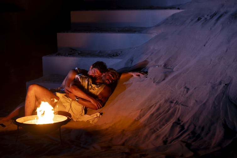 Two men embrace near a fire.