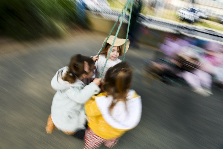 Three young children play on a swing together