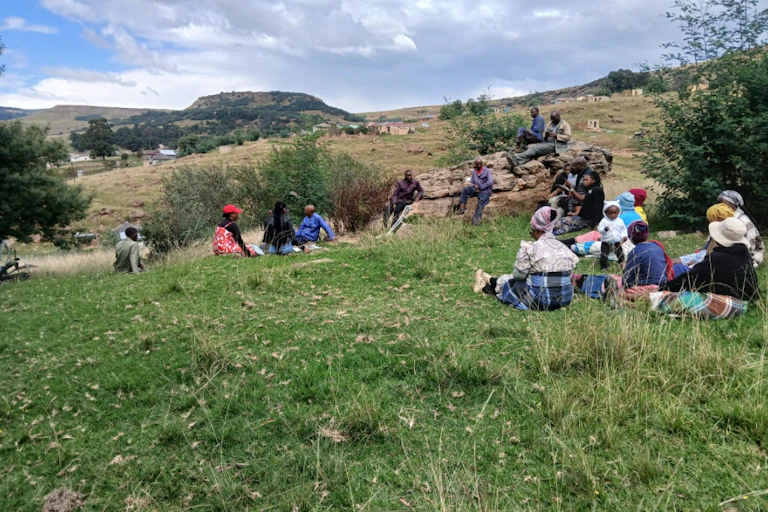 Rolling green and brown hills with a dozen people sitting down on the grass
