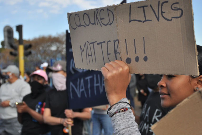 A woman in a crowd holding up a cardboard placard written 'Coloured Lives Matter'
