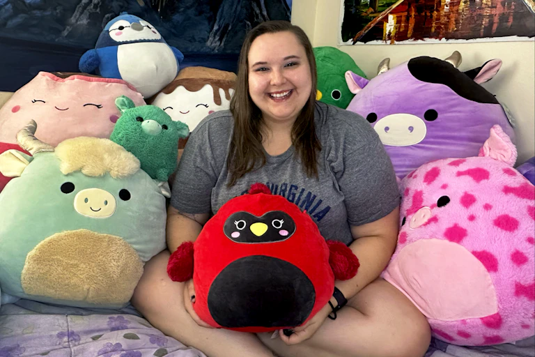 A smiling professor is surrounded by large plush toys. She holds a stuffed cardinal, a personal symbol of her father, in her lap.