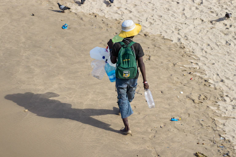 View from above of a man walking along a beach, carrying plastic bottles