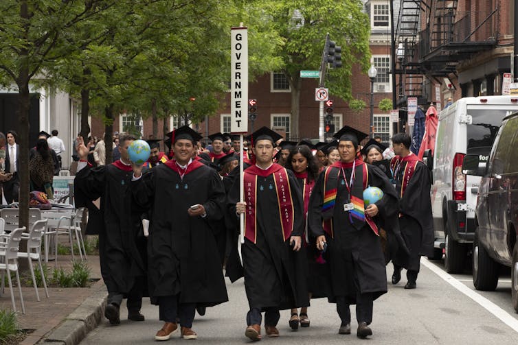 A group of young people wear black robes and black graduation hats and walk together. Some of the people hold globes.