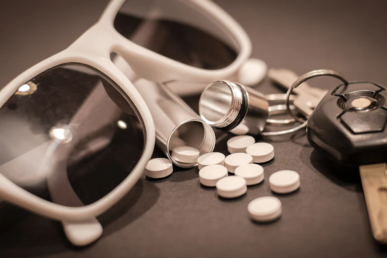 Black and white image of sunglasses, spilled pills and keys sitting on a counter