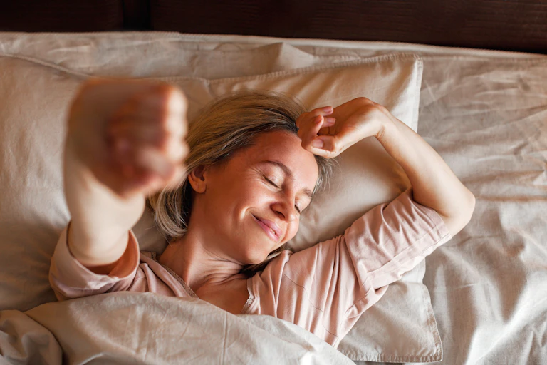A woman smiles as she stretches in bed