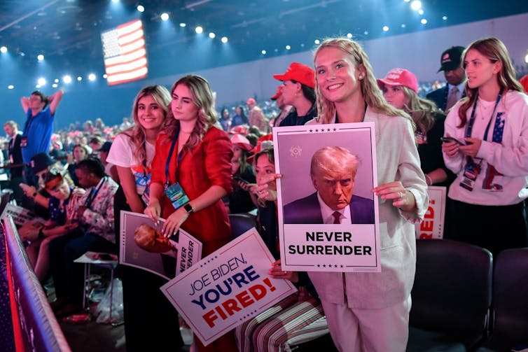 Young women in a crowd holding signs, including one that says 'Joe Biden You're Fired!'