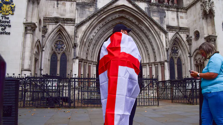 A man wrapped in an English flag standing outside the Royal Courts of Justice in London.