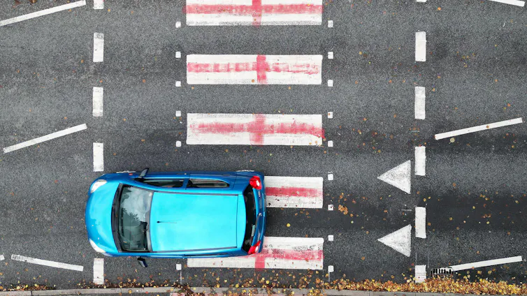 A car driving over a zebra crossing that has been painted as St George's flags.