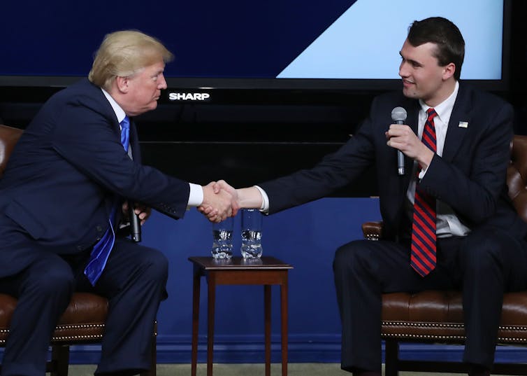 Two men shaking hands while sitting on a stage.