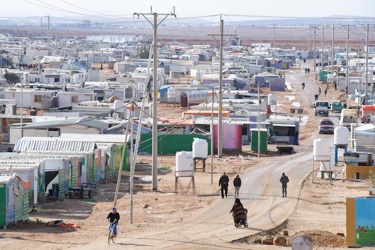 People and cars on a road running through a refugee camp in Jordan.