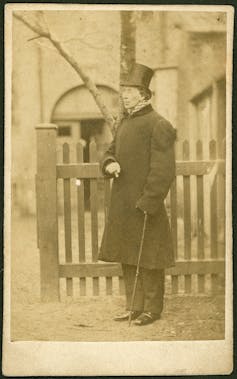 Sepia: una fotografía de un hombre con un abrigo, sombrero y bastón.